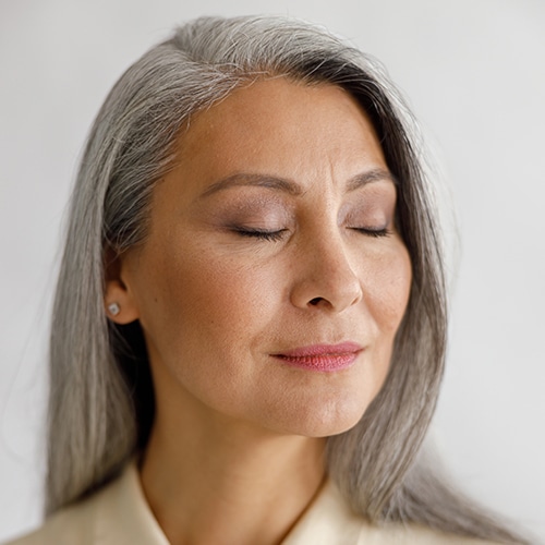 Calm middle aged woman with closed eyes stands on light background Mujer bella